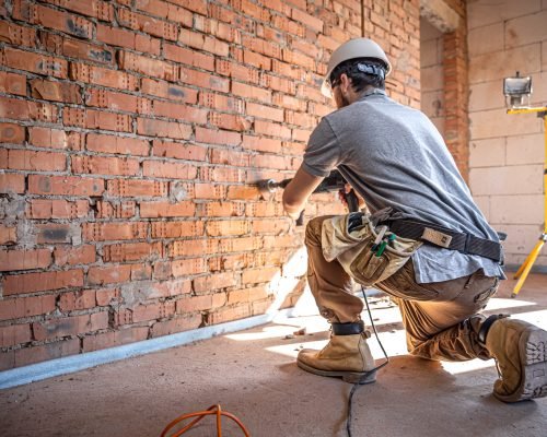 Handyman at a construction site in the process of drilling a wall with a perforator.